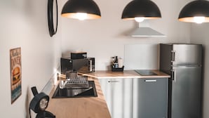 A modern kitchen with a built-in dishwasher, a stainless steel refrigerator, and a coffee maker on the counter. - Résidence des Sables (Mably)