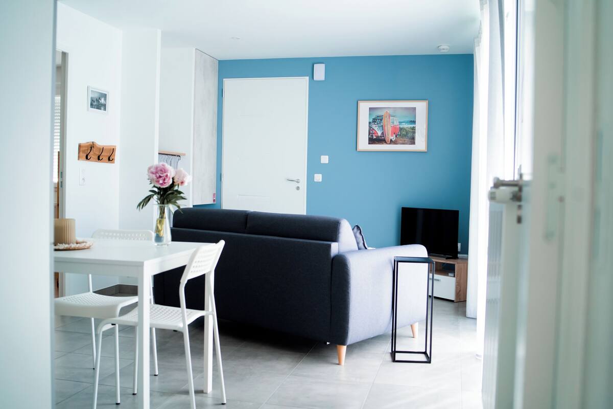 A modern living room with a sofa, a dining table with chairs, and a TV.