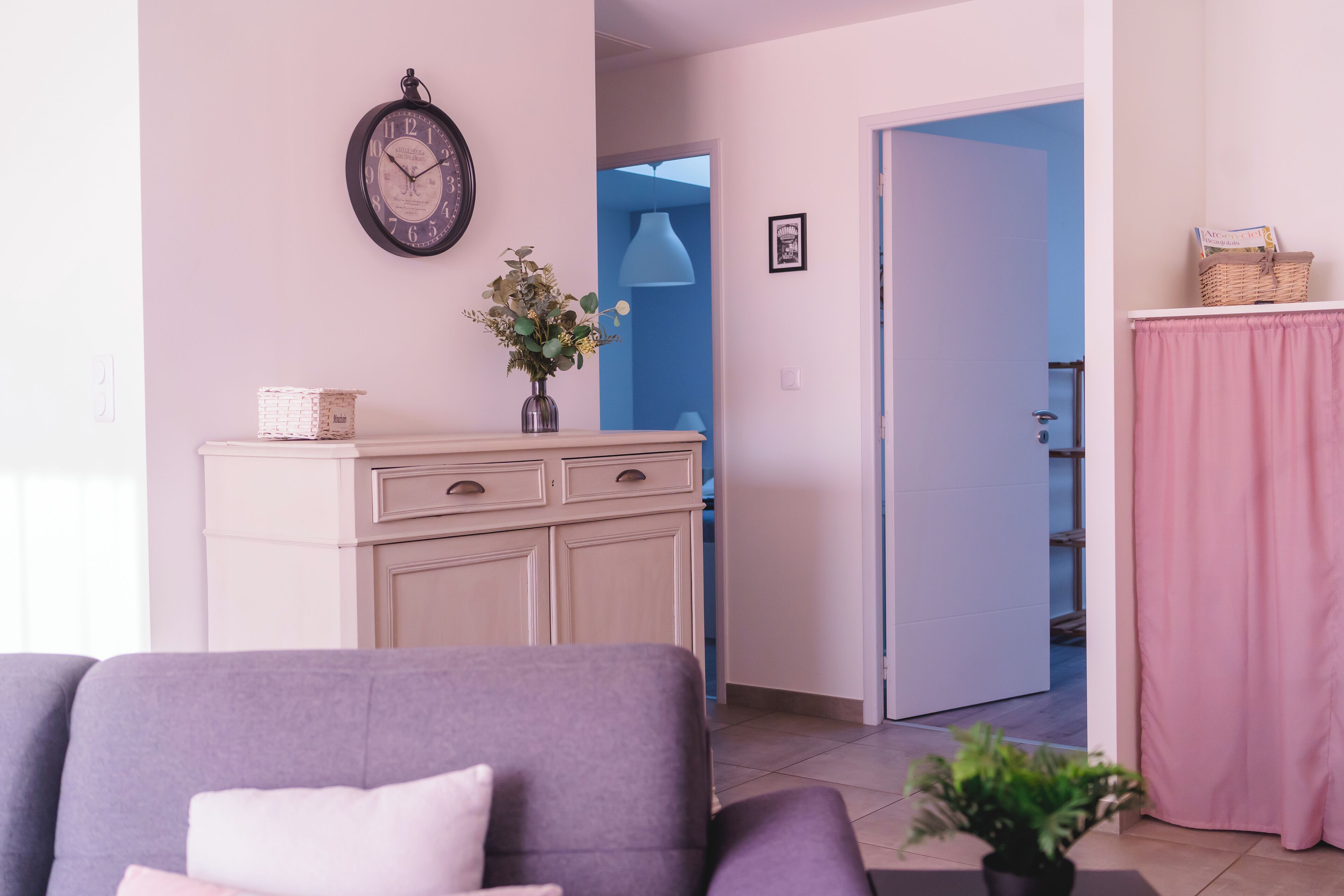 Ein Wohnzimmer mit einer Couch, einem Schrank, einer Uhr und einem Durchgang zu einem anderen Raum.
