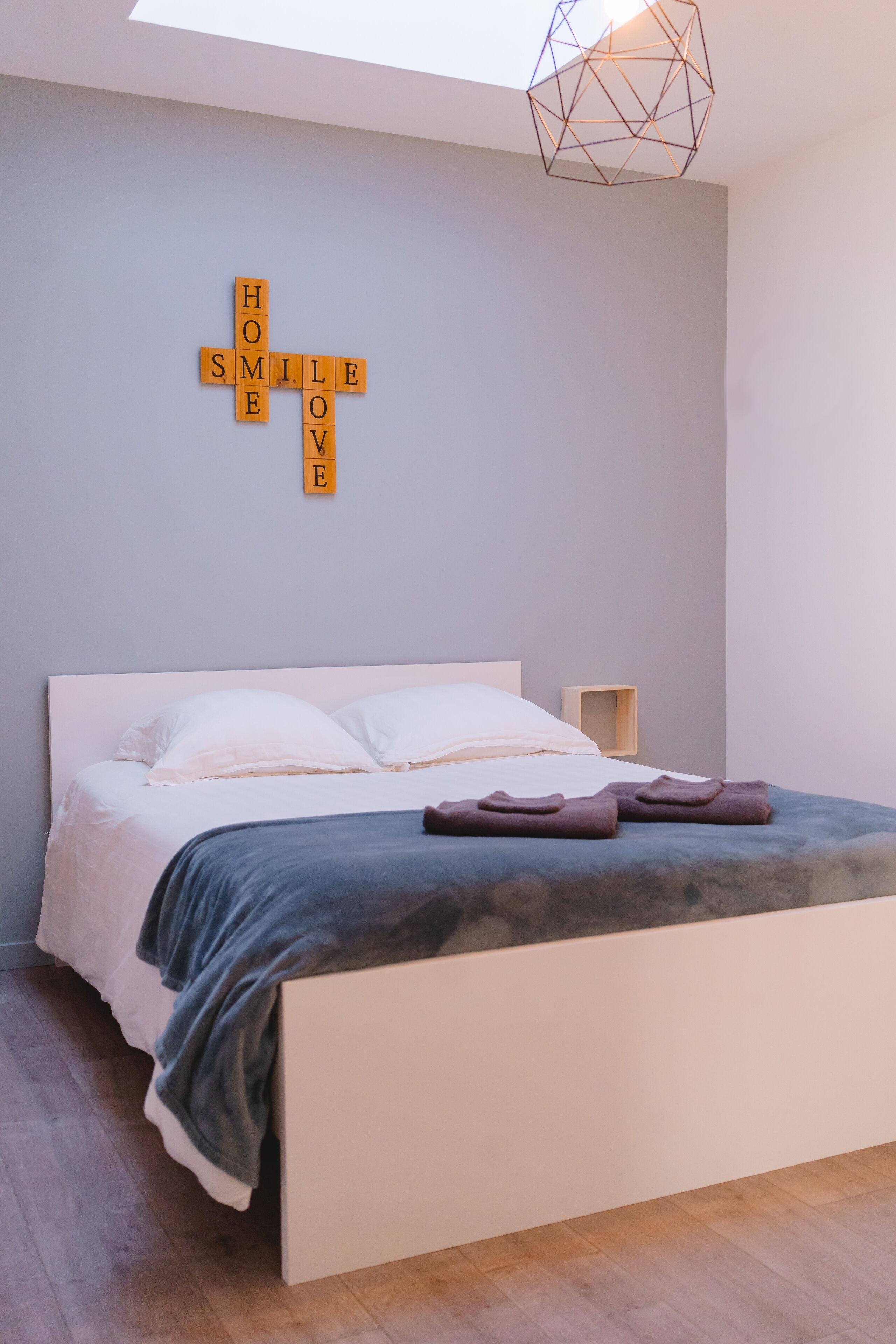 Un dormitorio moderno con una cama, almohadas, una mesita de noche y una lámpara con diseño geométrico.
