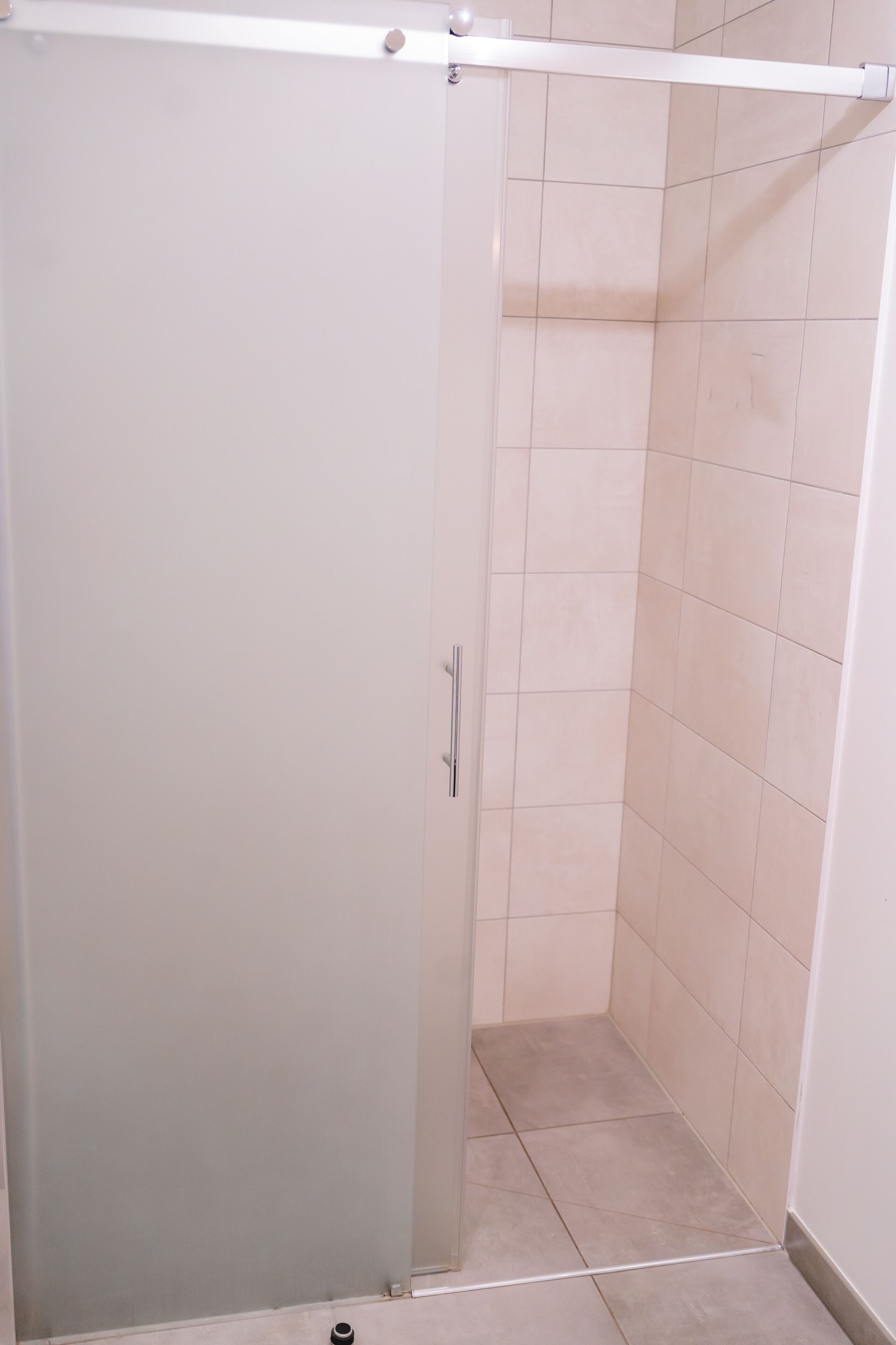 Un área de ducha pequeña y cerrada con puerta de cristal y paredes de azulejos.