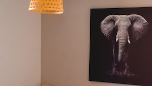 A bedroom with a bed, a nightstand, a lamp, and a wall-mounted elephant artwork. - Résidence des Sables (Mably)