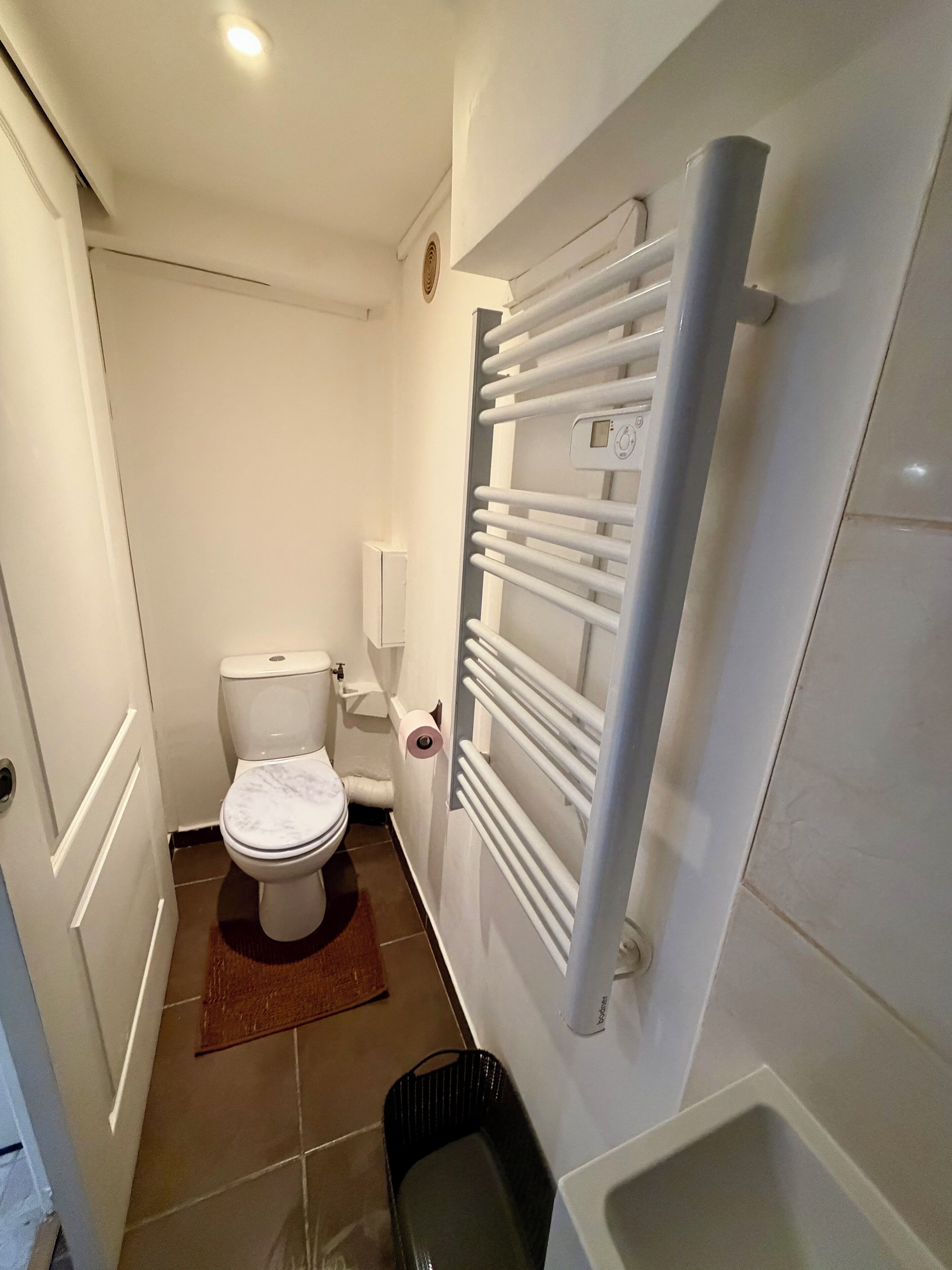 A small, modern bathroom with a toilet, a white radiator, and a black trash bin.