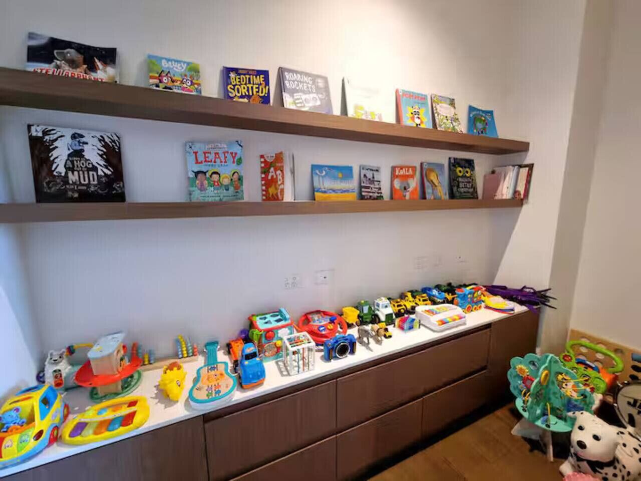 A room with a bookshelf filled with children's books and a long table with various toys and playsets.