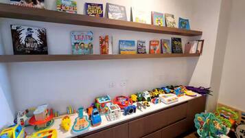 A room with a bookshelf filled with children's books and a long table with various toys and playsets.