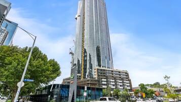A modern high-rise building with a glass facade, located at a street corner with a clear sky.