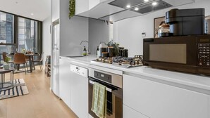 A modern kitchen with a built-in oven, microwave, and a dining area with a table and chairs. - Stylish Arts Apt | Lift | Gym | Sauna (Southbank)