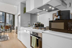 A modern kitchen with a built-in oven, microwave, and a dining area with a table and chairs. - Stylish Arts Apt | Lift | Gym | Sauna (Southbank)