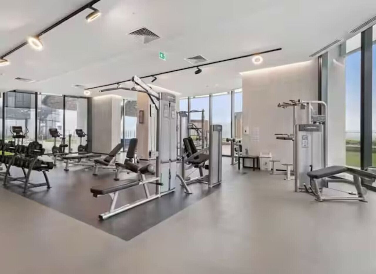A modern gym with various exercise equipment, large windows, and a clean, spacious layout.
