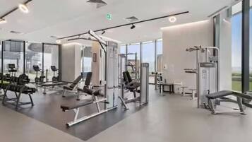 A modern gym with various exercise equipment, large windows, and a clean, spacious layout.