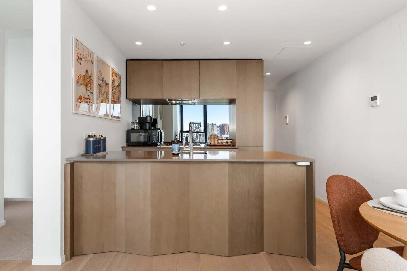 A modern kitchen with a central island, wooden cabinets, and a dining area with a table and chairs.