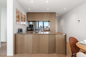 A modern kitchen with a central island, wooden cabinets, and a dining area with a table and chairs. - Amalfi Chic | Pool | Gym | Sauna (Southbank)
