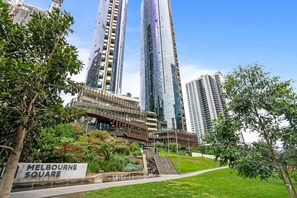 A modern building complex with a prominent vertical structure, a landscaped garden area, and a sign indicating 'Melbourne Square.'