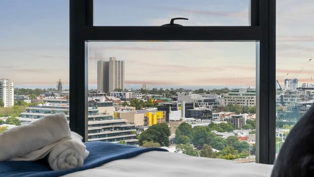 A bed with a view of a cityscape through a window.