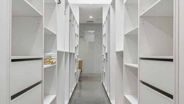 Ein schmales, weißes Dreibettzimmer mit integrierten Regaleinheiten an beiden Seiten, das zu einem Badebereich führt.