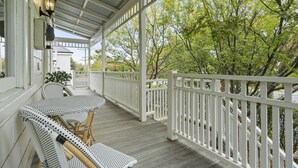 A covered porch with white railings, a table with chairs, and a view of trees.