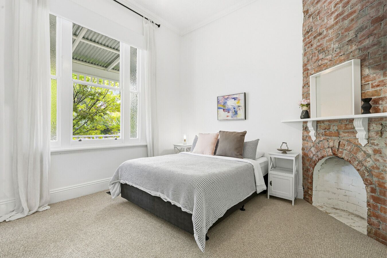 A bedroom with a bed, a nightstand, a fireplace, and a window with curtains.