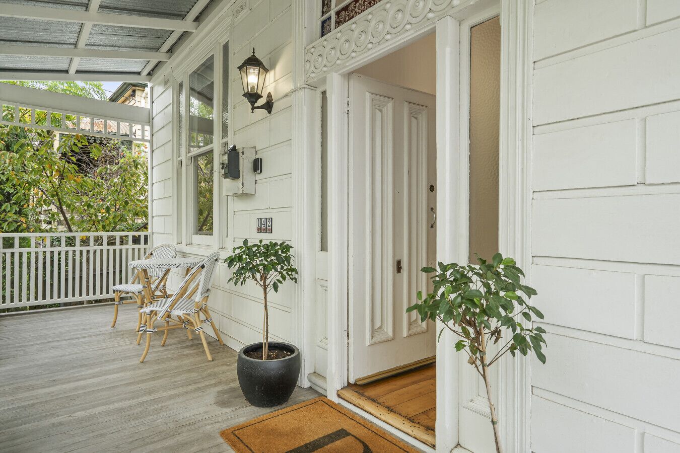 A covered porch with white railings, a wooden table and chairs, and two potted plants.