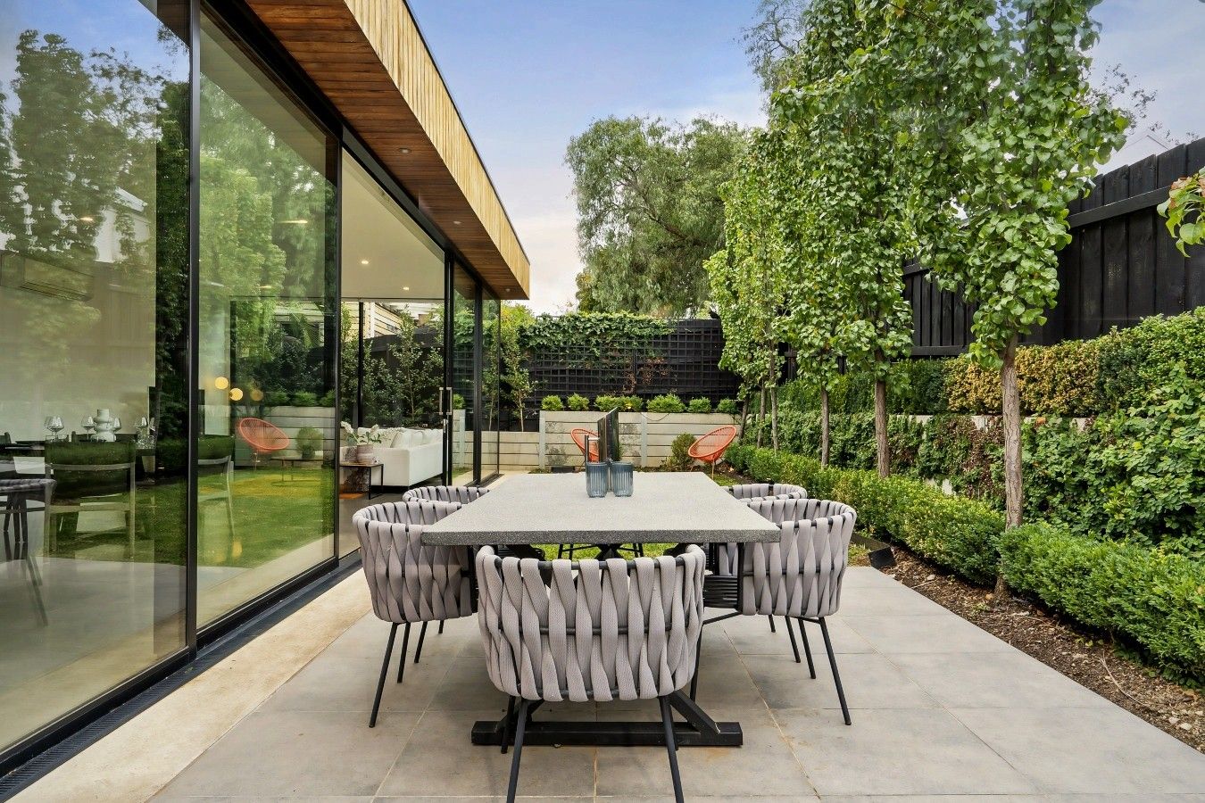 Een moderne eethoek buiten met een glazen wand, een houten plafond en uitzicht op een tuin.