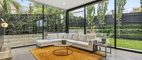 A modern living room with a white sectional sofa, a round coffee table, and a large window overlooking a garden.