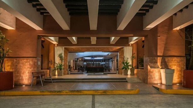 Un vestíbulo de hotel con diseño moderno, que cuenta con una zona de estar central, una recepción y plantas en macetas.