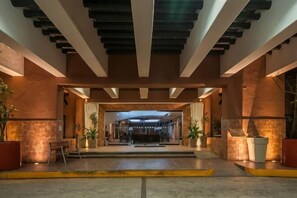 A hotel lobby with a modern design, featuring a central seating area, a reception desk, and potted plants. - Holiday Inn CD. DEL CARMEN by IHG (Ciudad Del Carmen)