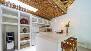 A modern kitchen with white cabinetry, a central island with stools, a built-in refrigerator, and a wooden ceiling. - The Oasis Villa (Kerobokan)