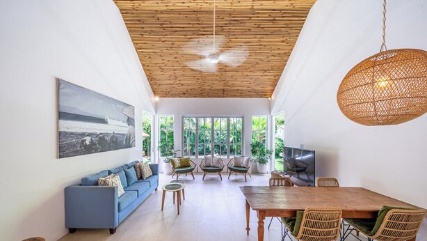 A spacious living area with a blue sofa, a wooden dining table, wicker chairs, and a television. - The Oasis Villa (Kerobokan)