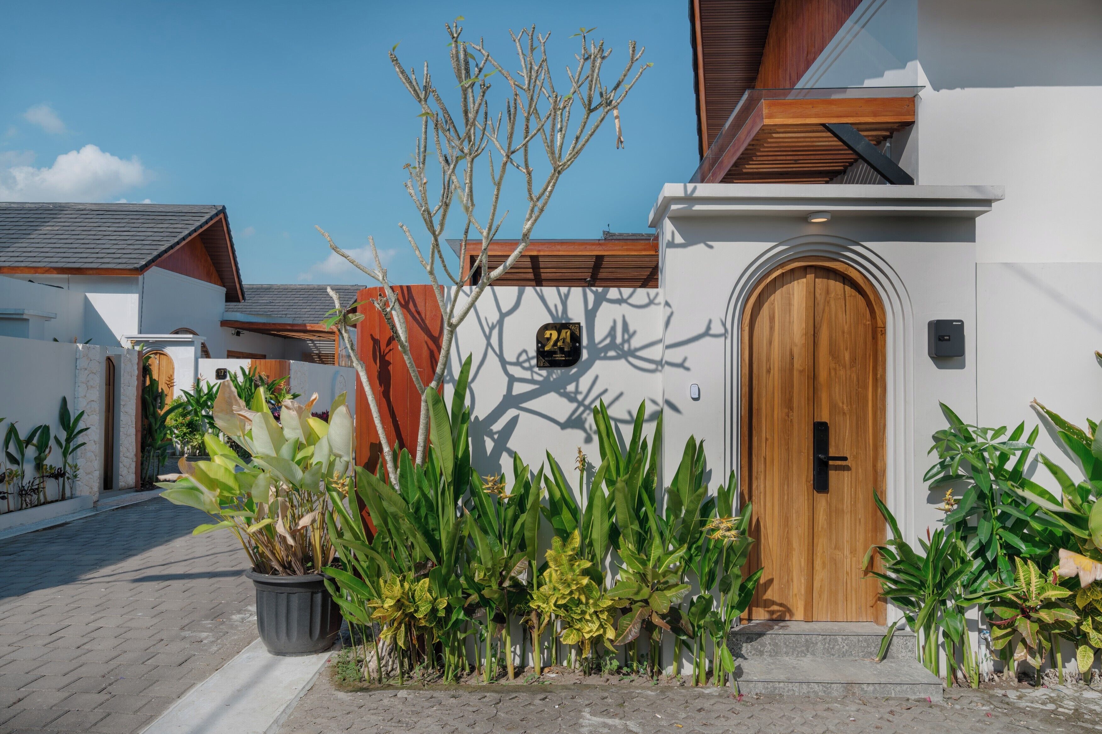A modern building with a wooden door, potted plants, and a clear sky.