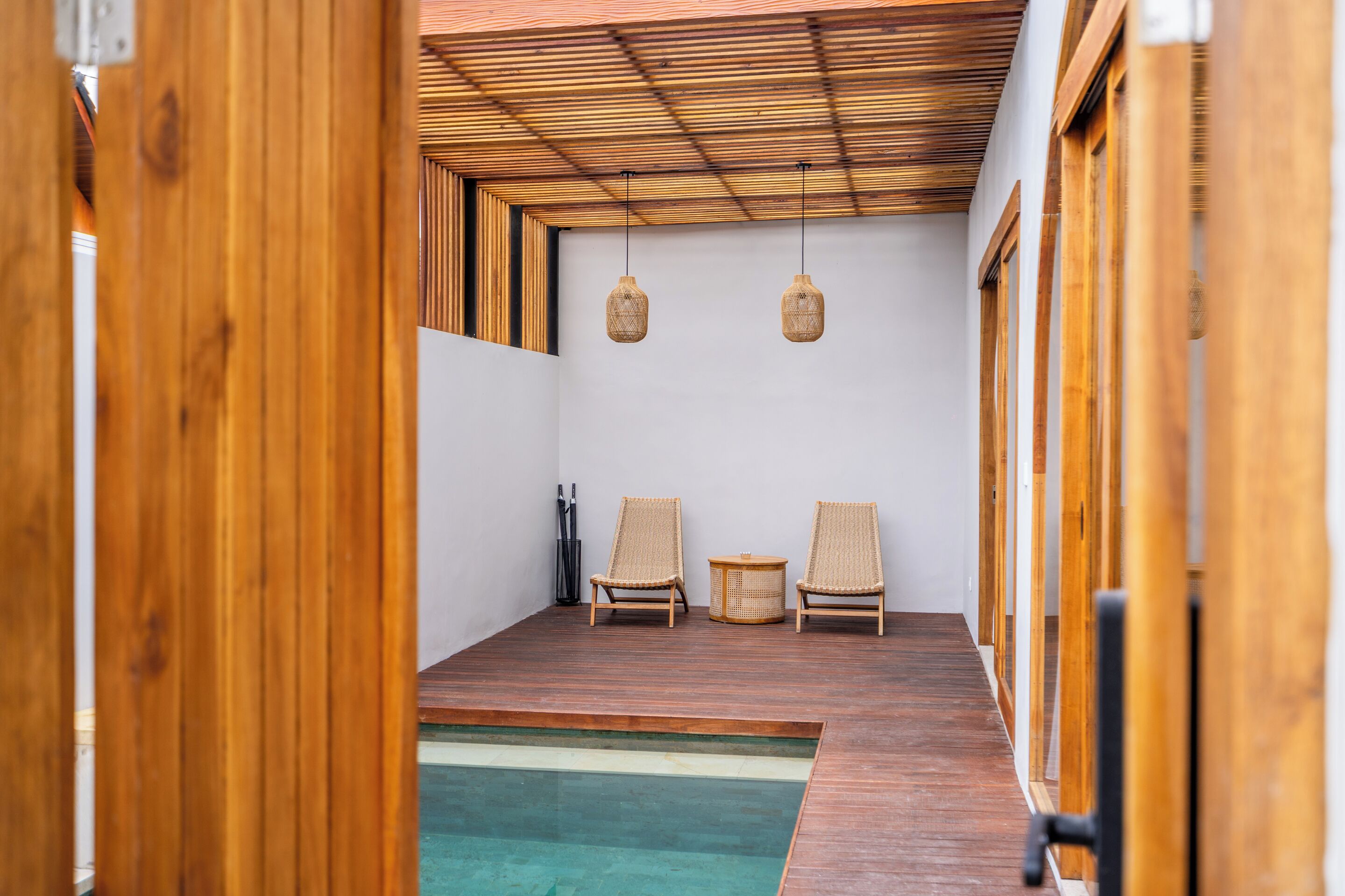 Ein kleiner Raum mit Holzboden, zwei Korbstühlen und einem Tisch, Holzbalkendecke und einem Schwimmbecken.