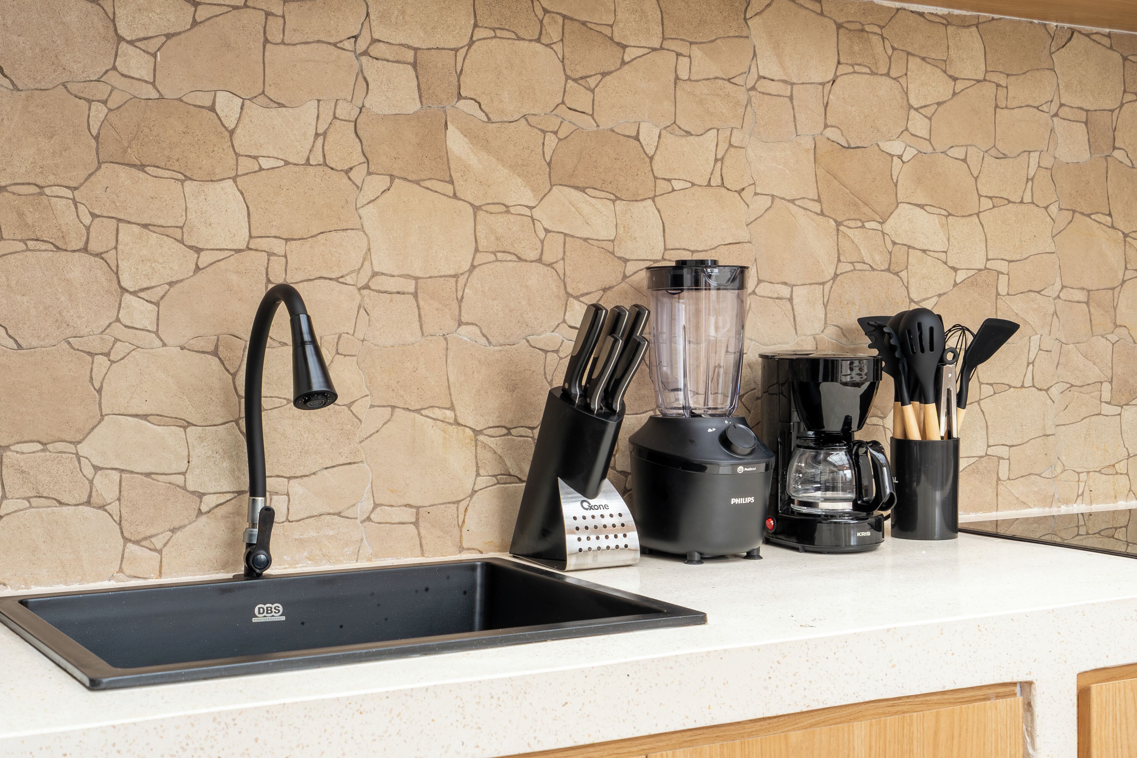 A kitchen with a stone backsplash, a black sink, a blender, and a coffee maker.