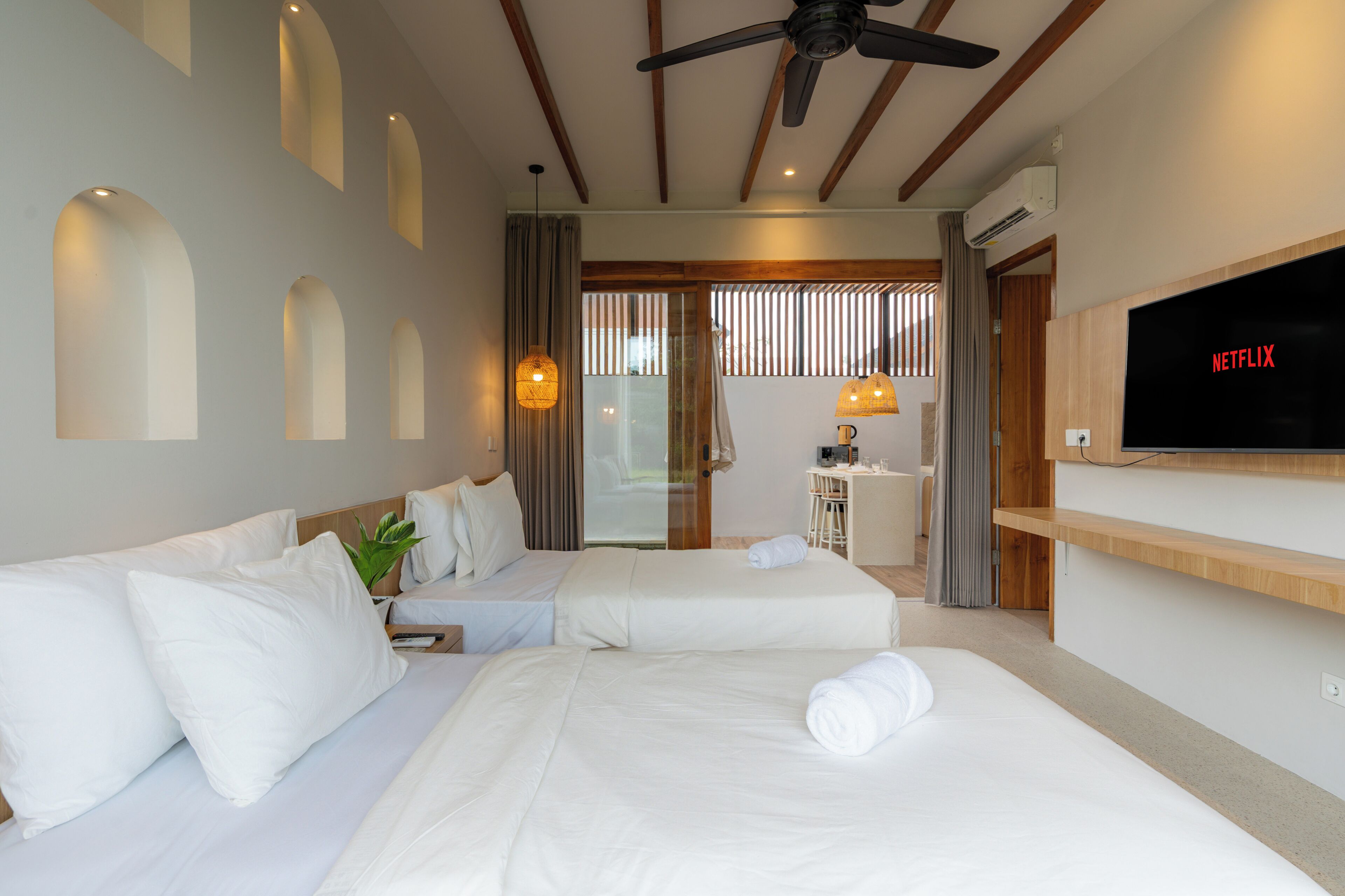 A hotel room with two beds, a TV, a ceiling fan, and a view of the outside.