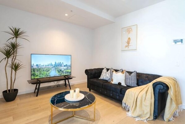 A living room with a sofa, a coffee table, a TV, and a potted plant. - 1B1B Condo with Bay &River Views (Docklands)