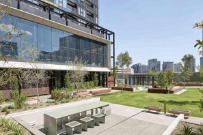 A modern building with large glass windows, outdoor seating, and a well-maintained lawn. - 1B1B Condo with Bay &River Views (Docklands)