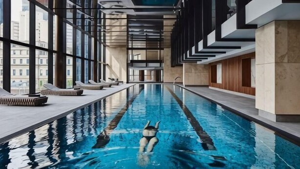 Ein Schwimmbecken mit einer schwimmenden Person, umgeben von moderner Architektur und großen Fenstern.