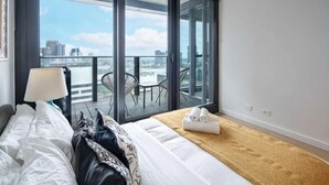 Ein Hotelzimmer mit Bett, Nachttisch, Lampe, einem Balkon mit Sitzgelegenheiten und Blick auf die Stadt.