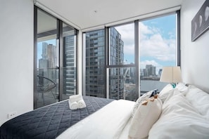 A hotel room with a bed, a chair, a window with a city view, and a balcony. - 1B1B Condo with Bay &River Views (Docklands)