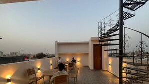 Terraço no telhado com mesa redonda e cadeiras, escada e vista da cidade.