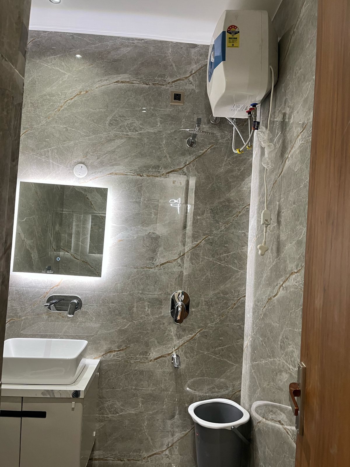 A bathroom with a marble wall, a built-in sink, a mirror, and a toilet.