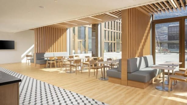 A modern interior with wooden flooring, a patterned rug, and a mix of seating areas including sofas and tables. - Holiday Inn Express & Suites SION by IHG (Sion)