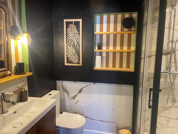 Une salle de bain moderne avec un lavabo en marbre, des toilettes, une douche et un élément décoratif en forme de feuille fixé au mur.