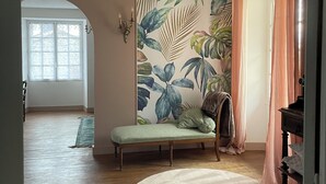 Une pièce dotée d’une grande fenêtre, d’un banc, d’un tapis rond et d’un mur orné d’un motif de feuilles tropicales.