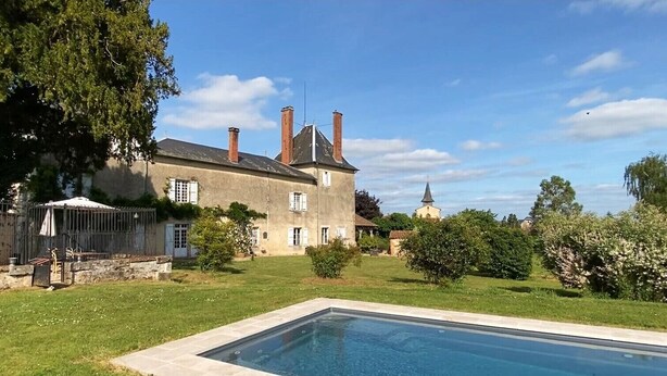Une grande maison avec une piscine, entourée de verdure, et une petite église en arrière-plan.