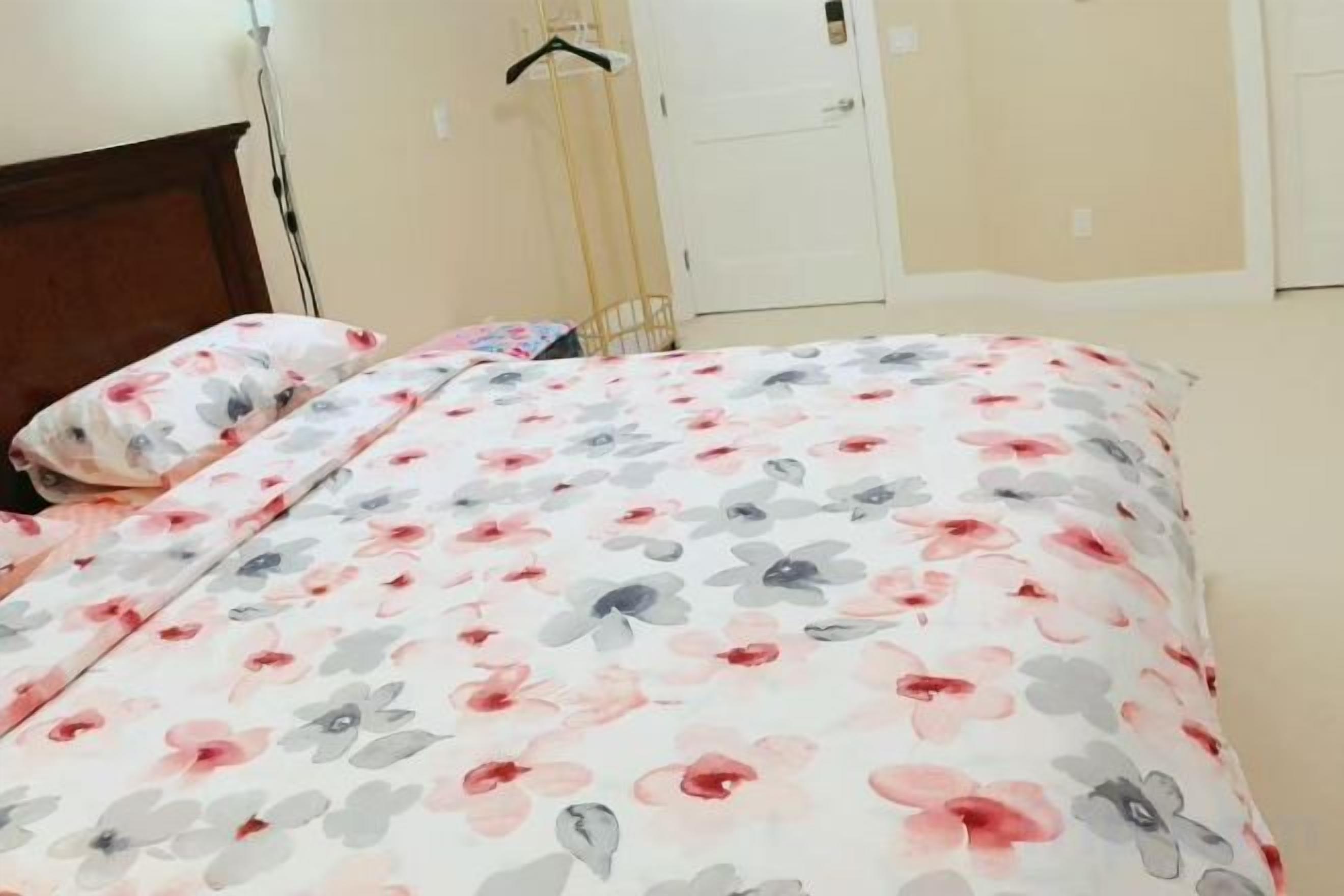 A bed with a floral bedspread and a matching pillow, a wooden headboard, and a white door in the background.