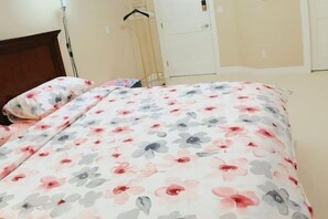 A bed with a floral bedspread and a matching pillow, a wooden headboard, and a white door in the background. - Derbyshire House Coquitlam Quiet, Clean & Comfortable · Free Parking (Coquitlam)