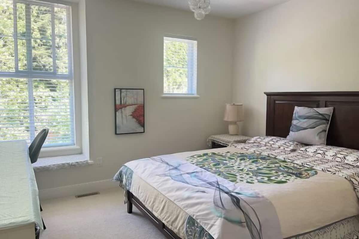A bedroom with a large bed, a nightstand, a chair, and two windows.
