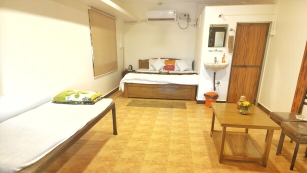 A room with two beds, a wooden table, a sink, and a mirror. - Ganesh Agro Tourism (Rajapur)