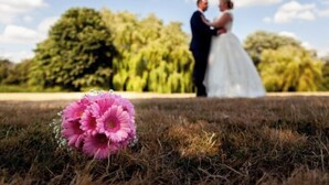Een trouwkoppel buiten, met een boeket roze bloemen op de voorgrond.