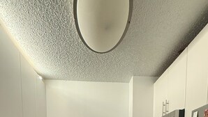 A compact kitchen with white cabinets, a stainless steel refrigerator, a microwave, and a stove. - Newport Apartment (Jersey City)