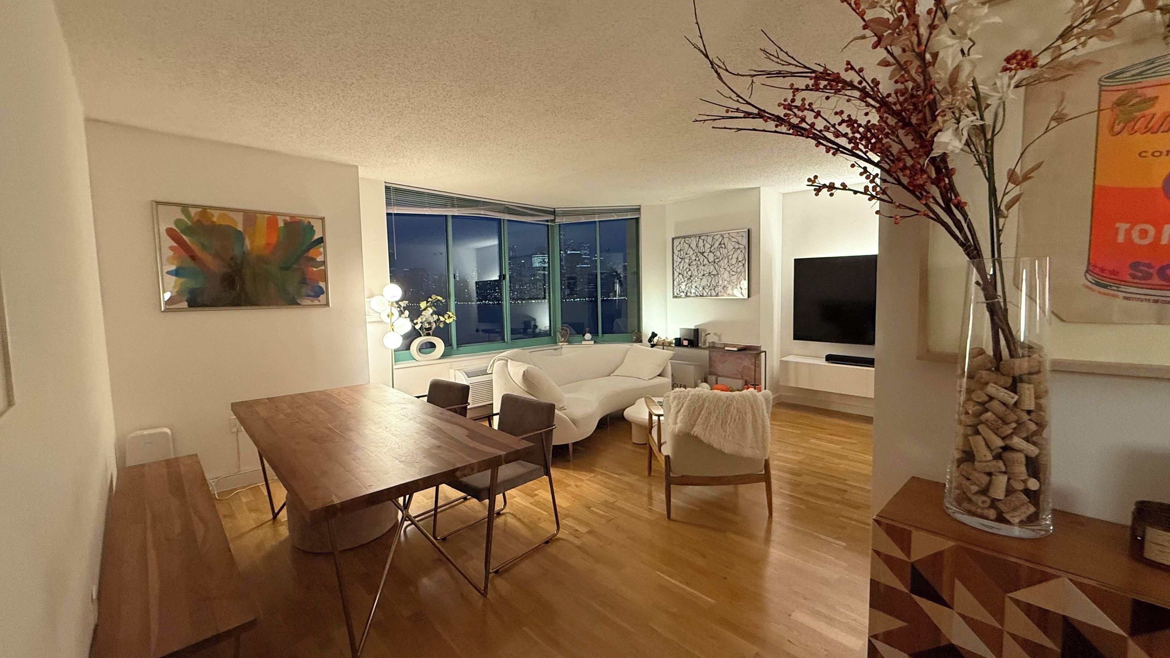 Een woonkamer met een eettafel, een witte bank en een televisie.